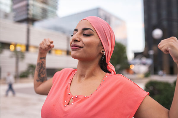 Smiling woman in pink headscarf and shirt flexes muscles in triumph