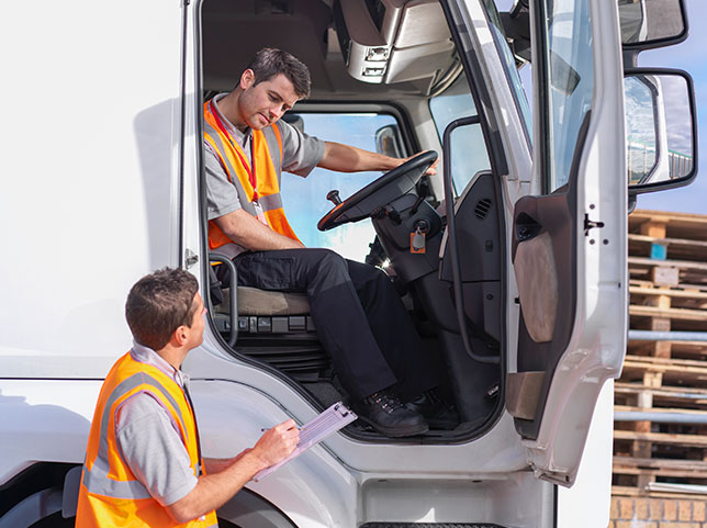 Two employees in safety vests converse from cab of truck