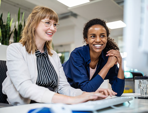 Two smiling co-workers look together at computer screen