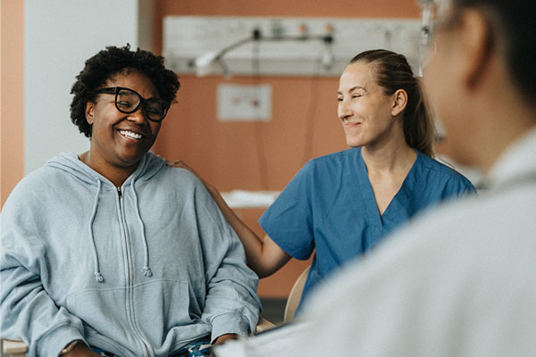 Nurse compassionately puts arm on shoulder of smiling patient in clinical setting