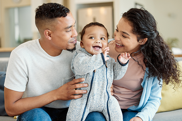 Happy parents sit on couch holding smiling baby