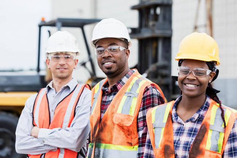 three smiling construction workers stand together at work site