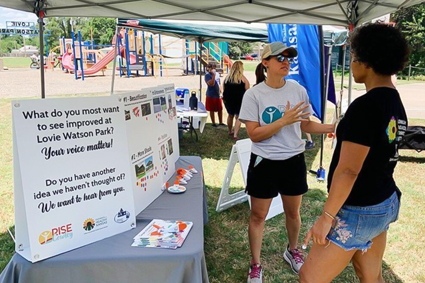 Rise Cowley representative speaks with guest at outreach booth in Lovie Watson Park