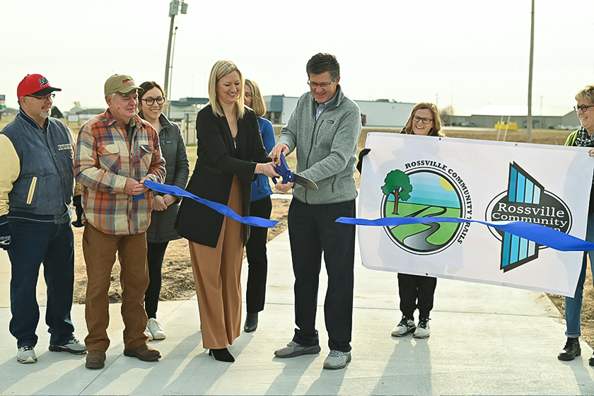 Two people use large scissors to cut blue ribbon for trail opening