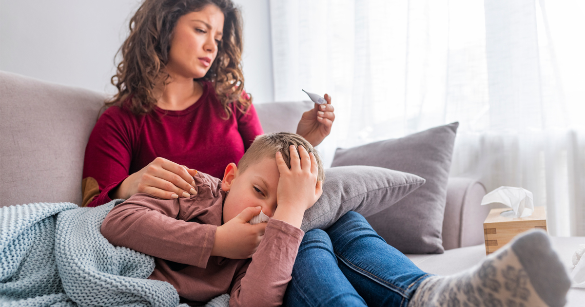 A mother reads a thermometer while comforting her sick child