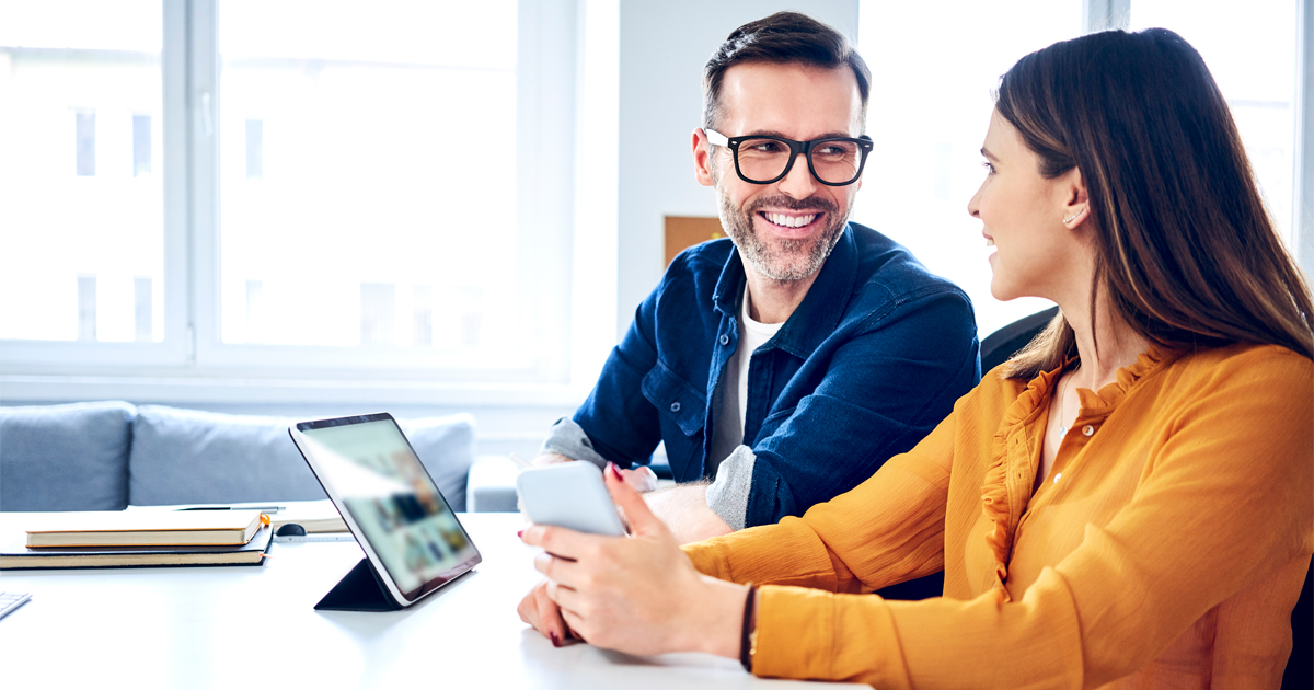 A woman holding a phone talking to a man with a tablet computer.