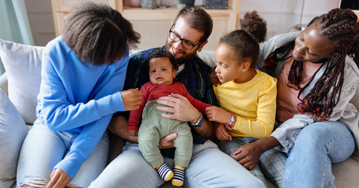 A family on a couch interacts with a baby