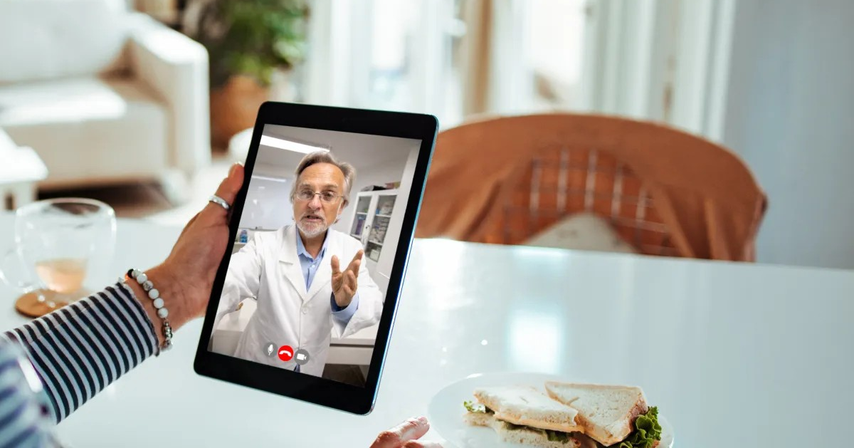 A patient holds a tablet computer and talks to a doctor on the tablet screen.