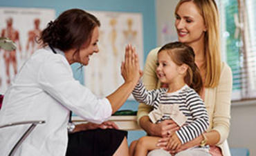 A mother holding her daughter on her lap who is giving the doctor a high five