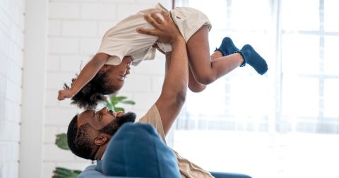 A reclined smiling man holds a smiling child above his head