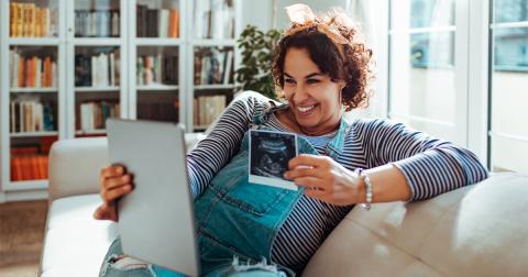 Smiling woman showing ultrasound photo to tablet device camera