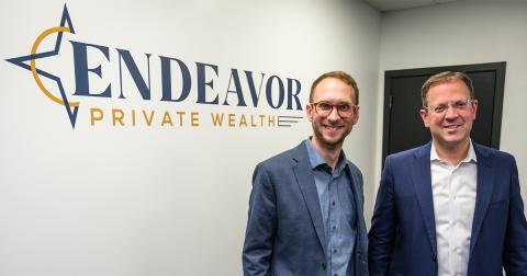 Two men in suits stand in front of a sign reading 'Endeavor Private Wealth'