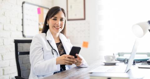 A doctor sits at a desk holding her mobile phone