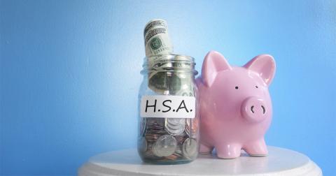 A piggy bank next to a mason jar full of money. The jar has a label that reads 'H. S. A.'