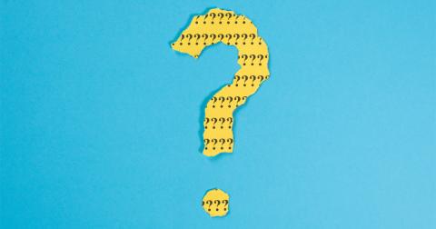 A question mark formed out of torn yellow paper with black question marks printed on it.