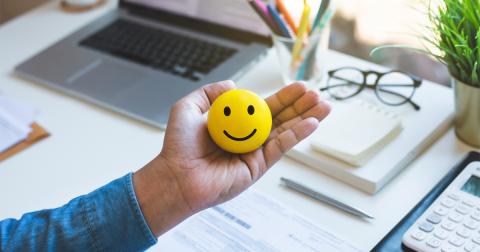 A smiley face held in a hand above a work desk