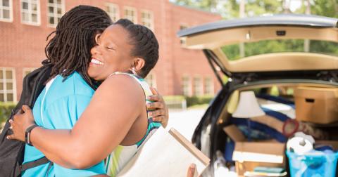 A mother hugs her child while unpacking a car at college